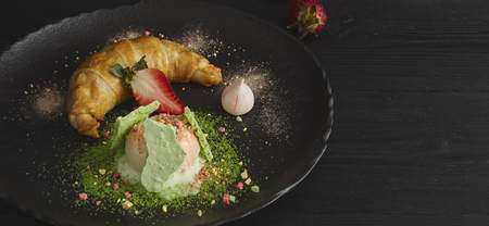 Slice of apple strudel with a scoop of vanilla ice cream on a black plate, on a wooden black table, decorated with meringue and strawberries. close-up. horizontal view of bakedの写真素材