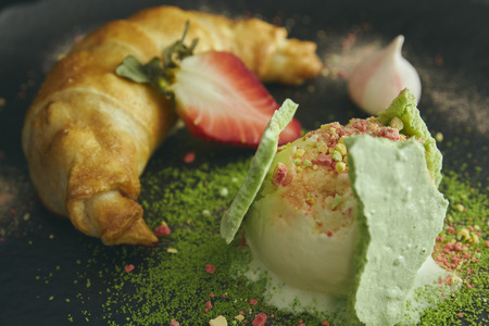 Slice of apple strudel with a scoop of vanilla ice cream on a black plate, on a wooden black table, decorated with meringue and strawberries. close-up. horizontal view of bakedの写真素材