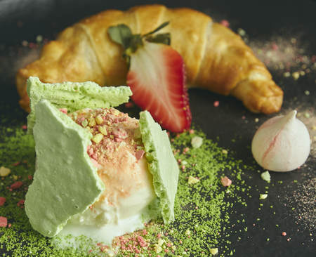 Slice of apple strudel with a scoop of vanilla ice cream on a black plate, on a wooden black table, decorated with meringue and strawberries. close-up. horizontal view of bakedの写真素材
