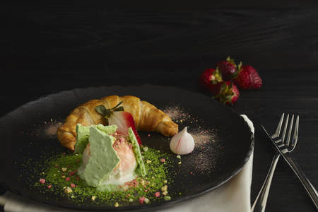 Slice of apple strudel with a scoop of vanilla ice cream on a black plate, on a wooden black table, decorated with meringue and strawberries. close-up. horizontal view of bakedの写真素材