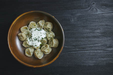 pelmeni with butter and greens on a black wooden table. Russian traditional dish of dough and minced meat. close up photo.の写真素材