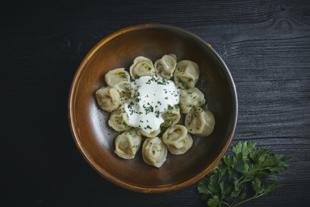 pelmeni with butter and greens on a black wooden table. Russian traditional dish of dough and minced meat. close up photo.の写真素材