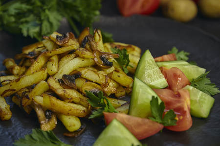 Freshly cooked fried potatoes with onions and mushrooms close-up on a plate. black wood table. horizontalの写真素材