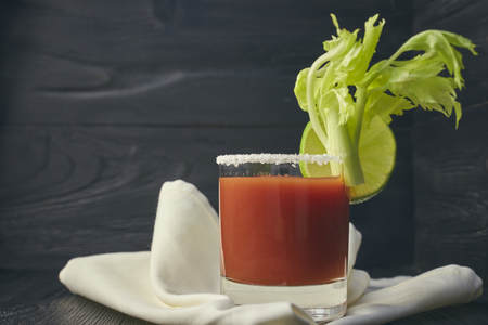 Cocktail Bloody Mary with lime and celery, salt and snacks in a glass on a black wooden table.の写真素材
