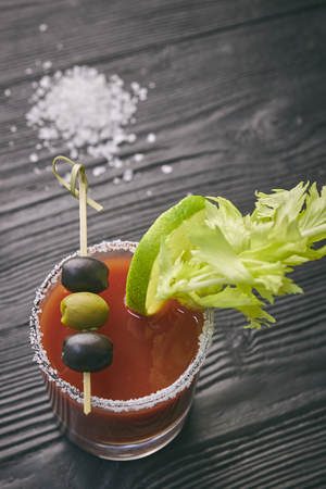 Cocktail Bloody Mary with lime and celery, salt and snacks in a glass on a black wooden table. vertical viewの写真素材