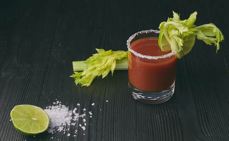 Cocktail Bloody Mary with lime and celery, salt and snacks in a glass on a black wooden table.の写真素材