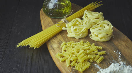 Set of raw pasta frame. Uncooked spaghetti, fusilli, fettuccine on a dark wooden background, horizontal view. close-up.の写真素材