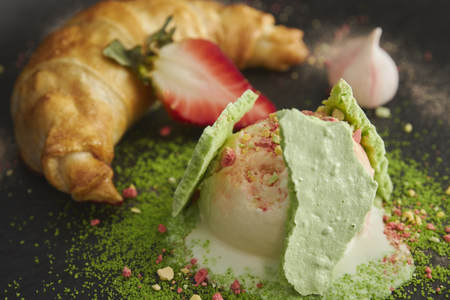 Slice of apple strudel with a scoop of vanilla ice cream on a black plate, on a wooden black table, decorated with meringue and strawberries. close-up. horizontal view of bakedの写真素材