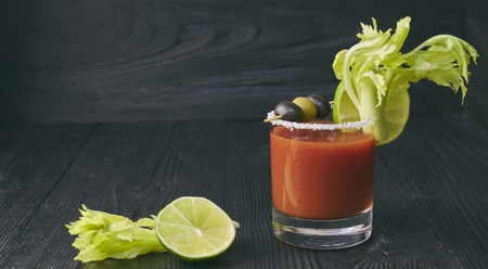 Cocktail Bloody Mary with lime and celery, salt and snacks in a glass on a black wooden table.の写真素材