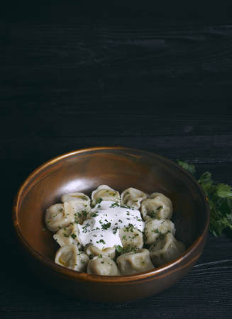 pelmeni with butter and greens on a black wooden table. Russian traditional dish of dough and minced meat. close up photo.の写真素材