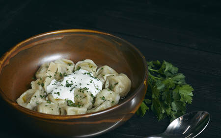 pelmeni with butter and greens on a black wooden table. Russian traditional dish of dough and minced meat. close up photo.の写真素材