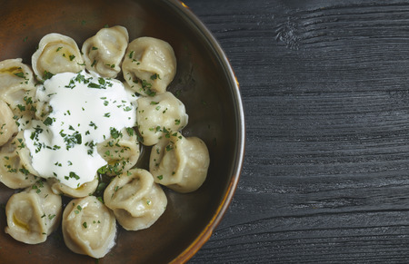 pelmeni with butter and greens on a black wooden table. Russian traditional dish of dough and minced meat. close up photo.の写真素材