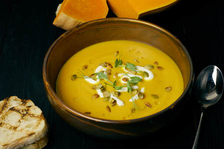 Pumpkin soup in a bowl with cream and pumpkin seeds. Vegan soup. Dark wooden backgroundの写真素材