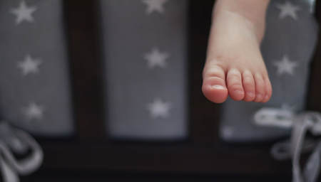 The child is sleeping in bed, his leg is hanging down. leg of a little