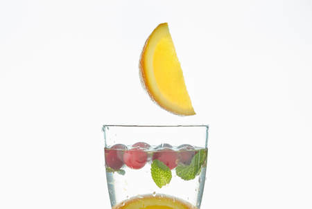 orange splashing into a glass of water with mint and berries on a white background. refreshing summer drink with citrus.の写真素材