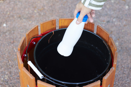 Woman's hand throws empty plastic water bottle into city street trash can on sunny day, close-upの写真素材