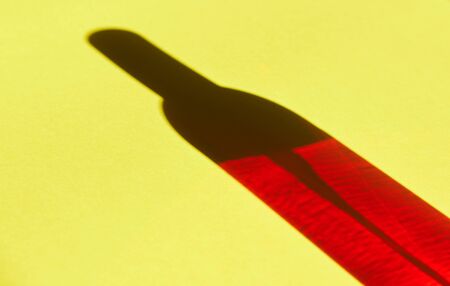 red shadow from a perfume bottle on a yellow background, shadow effects. shadow casting effects. cosmetics concept.の写真素材