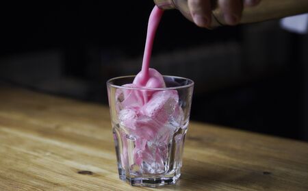 Bartender pouring a strong alcoholic drink into small glasses with ice. Red alcoholic drink. Barman is preparing a cocktail shooterの写真素材