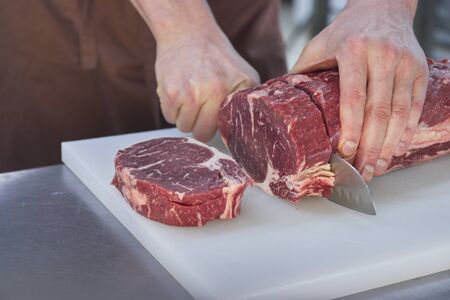 Butcher cutting beef in the kitchen. Closeup of hands with a knife and meat.の写真素材