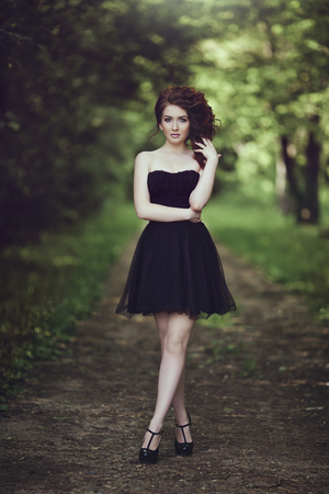 Beautiful young brunette girl in short black dress walking in the park. Little black dress.の写真素材