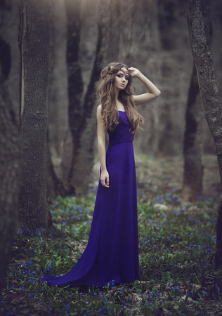 Girl elf with long hair and blue eyes in tiara and a long blue dress with a train walking through the spring blossoming forest. Girl Princess dreams.の写真素材