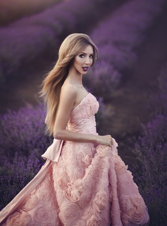 Beautiful sensual girl in lavender field at sunset. A woman in a gorgeous lush pink dress walks among the flowers of lavender. Provence.の写真素材