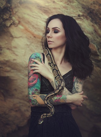 Portrait of brunette woman with tattoos posing with a snake. A girl in the desert with a Python.の写真素材