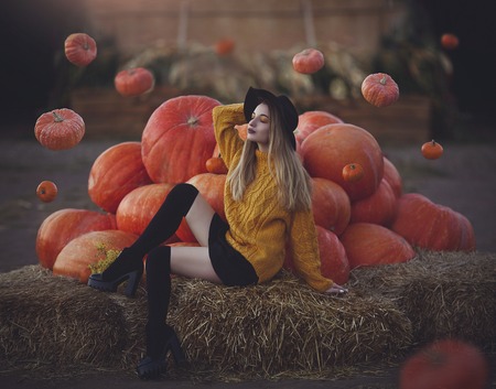 Modern young witch conjures levitating pumpkins. Beautiful girl in a hat near big pumpkins.の写真素材