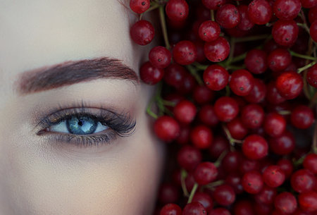 Close-up of a womans blue eye in red berries.の写真素材