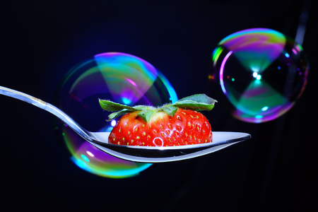 Big spoon with a slice of ripe strawberries with a peduncle, soap bubbles flying in the backgroundの写真素材