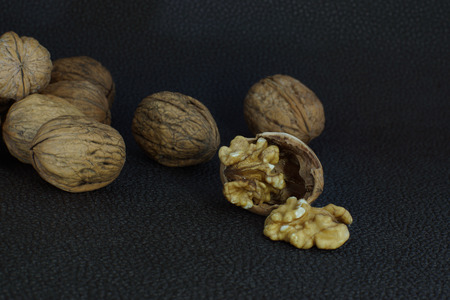 Walnuts lie in a heap on a dark background, one is split, half the shell and a kernelの写真素材
