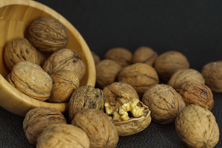 Walnuts are scattered from a bamboo bowl on a black background, one is uncovered.の写真素材
