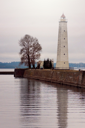 Tower lighthouse stands on the bank of a canal next to a tree, reflected in water.の写真素材