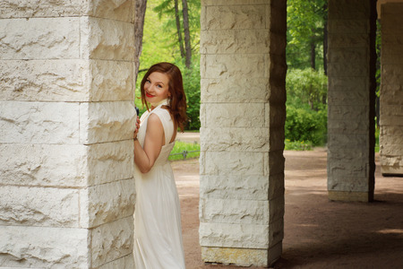A girl in a white dress peeks out from behind a columnの写真素材