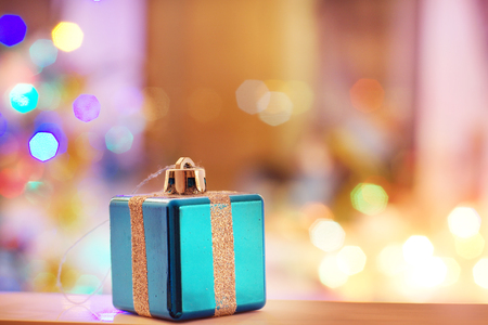New Year card with toy in the form of a gift with a ribbon on a background of blurred lights of the Christmas tree.の写真素材