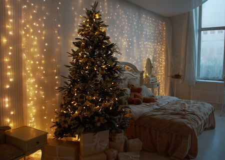 Interior of the bedroom, prepared for the New Year and decorated with a Christmas tree and gifts. Luminous garlands hang on the wallの写真素材