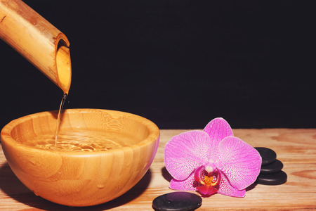 The jet of water is poured from the bamboo into a bowl on a wooden table, next to the spa treatment...