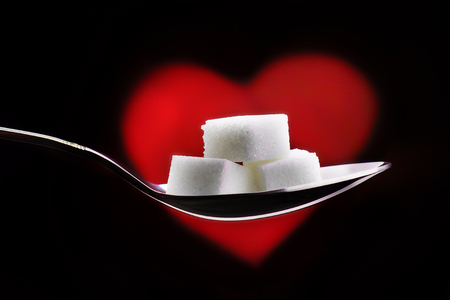 Three pieces of sugar lie on a spoon on a red heart background.の写真素材