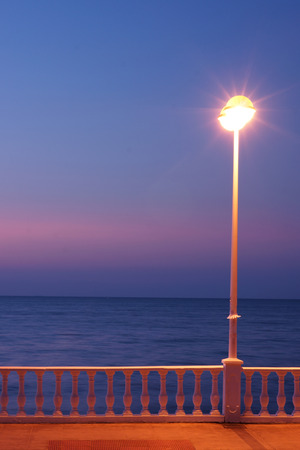 Glowing lantern and balustrade of the embankment near the sea in the morning at dawn.の写真素材