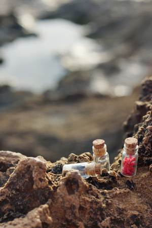 Small glass vessels with cork lids, filled with aromatic oil, salt and fragrant inflorescences on the rocks by the sea in the morning, spa set.の写真素材