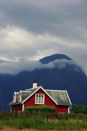 A bright red house stands behind a green fence against the backdrop of a formidable mountain in Norway.の写真素材