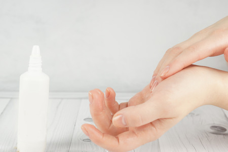 Female hands rub the cosmetic into the skin, next to the white flaconの写真素材