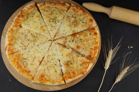 Cheese pizza, rolling pin for dough and stalks of wheat on a dark table, top view.の写真素材