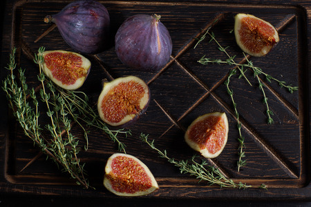 Ripe figs on a dark wooden board next to sprigs of thyme for tea.の写真素材