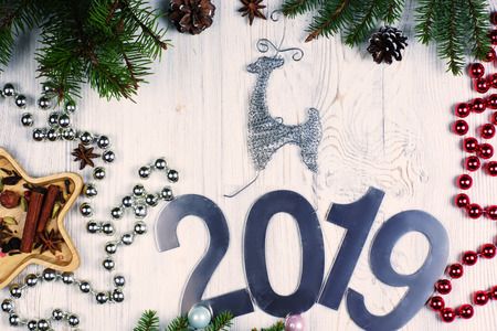 The inscription 2019 on a light wooden background on top of a deer, near shiny beads and fir branches with cones. New year concept. Greeting christmas card. Flat lay.の写真素材