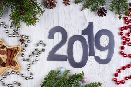 Figures 2019 on a light wooden background, near shiny beads and fir branches with cones. New year concept. Greeting christmas card. Flat lay.の写真素材