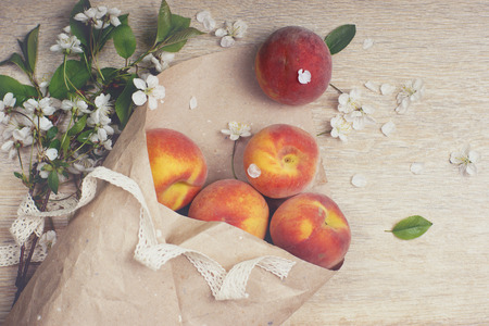 Ripe peaches are poured out of a package made from craft paper, next to a branch with white flowers, top view.の写真素材
