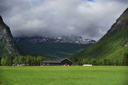Travel to Norway, a green field in front of a mountain range, over which hung a dark cloud with rain.の写真素材