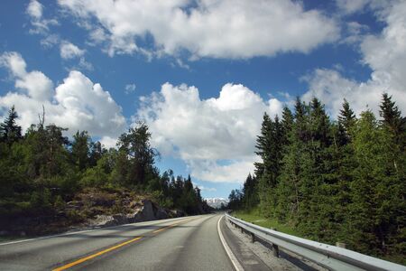 Travel to Norway, a direct asphalt road goes through the forest under a beautiful cloudy sky.の写真素材