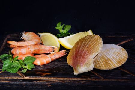 Shrimps and scallops in shells lie next to other ingredients before cooking